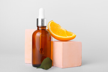 Bottle of essential oil and fresh orange on light background, closeup