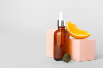 Bottle of essential oil and fresh orange on light background