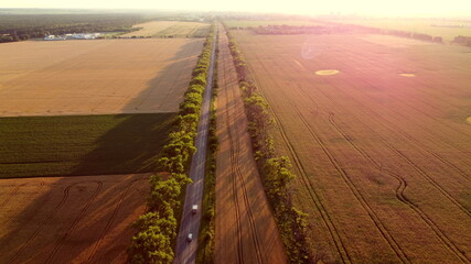 Drone flying over road between wheat fields during dawn sunset.