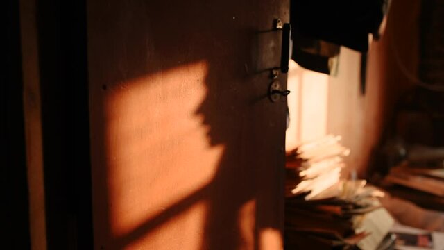 woman mouth silhouette talking saying in window shadow on orange door. attic loft interior. large stacks old newspapers. shadow silhouette people window from setting sun. sunset in old vintage room