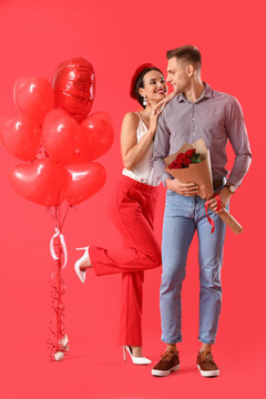 Happy young couple with bouquet of flowers and balloons on color background. Valentine's Day celebration