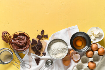 Bowl with fresh dough and ingredients for preparing chocolate brownie on yellow background