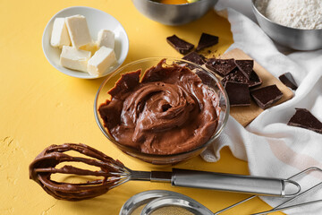 Bowl with fresh dough and ingredients for preparing chocolate brownie on yellow background