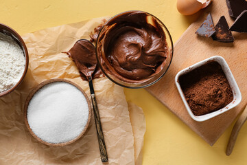 Bowl with fresh dough and ingredients for preparing chocolate brownie on yellow background