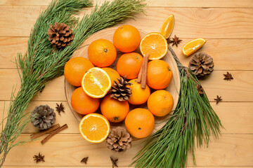 Plate with fresh oranges and fir branches on wooden background