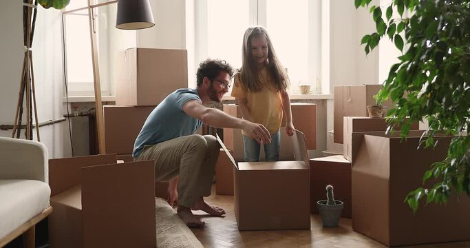 Happy playful little 6s girl jumping out cardboard box gives high five, enjoy playtime with loving father, celebrate relocation day to own flat. New house, homeowners family, move day, tenancy concept
