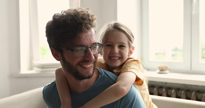 Close up portrait of happy young father and his little, cute daughter. Preschool girl piggy back his loving daddy, cheerful attractive family smile looking at camera. Bonding, fatherhood, bond concept