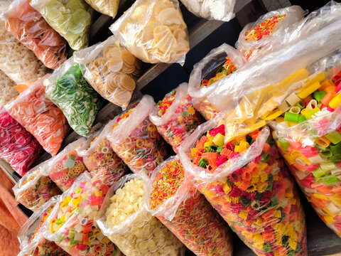 colorful raw fryums, papad, corn snacks, maida papad, khichiya papad, mix papad, maida fryums of different shapes, star, finger, round displayed in storefront for sale. ready to fry items.