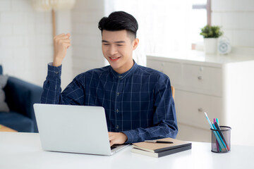 Happy young businessman work on laptop computer finish with excited and success on desk at home, business man using notebook with achievement and surprised, freelance or employee, satisfied and glad.