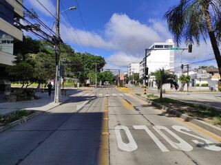Intersección de avenidas desiertas vacías con una parada de bus, árboles y palmeras, semáforos, señalética en la acera, y un hombre bajo un cielo despejado - obrazy, fototapety, plakaty