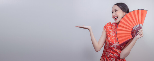 Asian woman in national dress of Chinese new year holding red wood fan with smiled and show hand to...