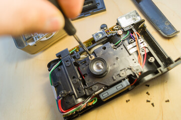 Fototapeta premium Repair of a compact camera. Unscrewing the screws on the camera parts with a screwdriver. Selective focus