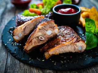 Tasty grilled ribs with french fries and fresh vegetables on wooden table
