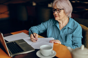 Senior woman with glasses sits at a table in front of a laptop Lifestyle unaltered