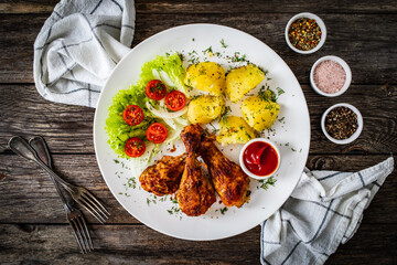 Barbecue chicken drumsticks with potatoes, lettuce and cherry tomatoes on wooden table