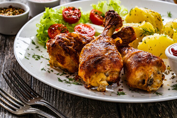 Barbecue chicken drumsticks with potatoes, lettuce and cherry tomatoes on wooden table