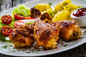 Barbecue chicken drumsticks with boiled potato, lettuce and mini tomatoes on wooden table