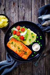 Fried salmon steak with potato puree and vegetable salad served on black plate on wooden table
