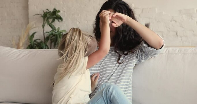 Close up of lively cheerful woman tickling her adorable daughter. Preschool 4s child girl sit on mommy laps enjoy playtime laughing have fun together at home. Bond and love, happy motherhood concept