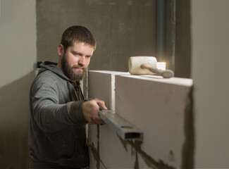 a male  builder puts a wall of aerated concrete in his house, in his hand  a level, he put it against the wall.