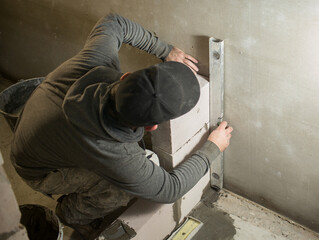 a male  builder puts a wall of aerated concrete in his house, in his hand  a level, he put it against the wall.