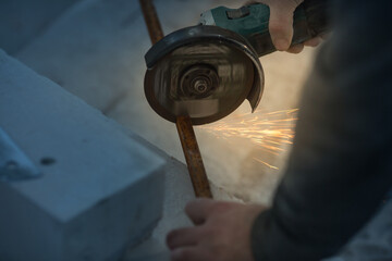 a man with a beard cuts a metal profile indoors with an angle grinder, sparks fly.