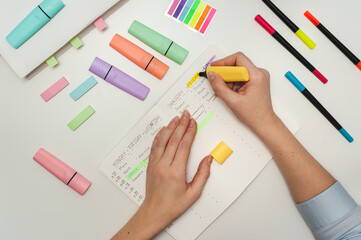 Planning the school year. Drawing up a student schedule. The girl makes edits with a yellow marker in the planner on the white table. Multicolored markers and stickers on a white table.