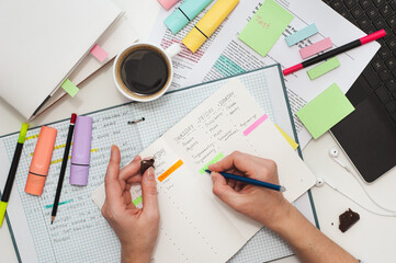 Student's desk. The girl makes notes on stickers in the study schedule. The process of homeschooling or preparing for lectures. Top view of the table with student stationery and notes.