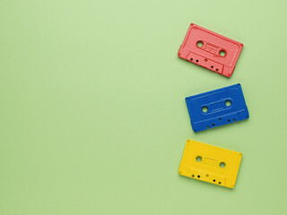 Three multi-colored tape cassettes on a light green background. Vintage style in sound recording.