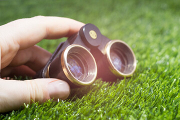 A small pair of binoculars in a woman's hand against a background of grass