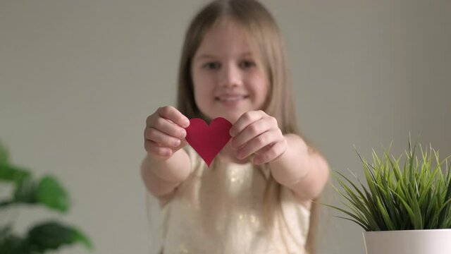 Small red heart close up in hands of little smiling girl on Valentines Day. Happy child with present for mothers or fathers day