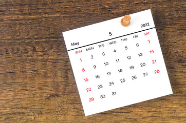 May 2022 calendar and wooden push pin on wooden background.