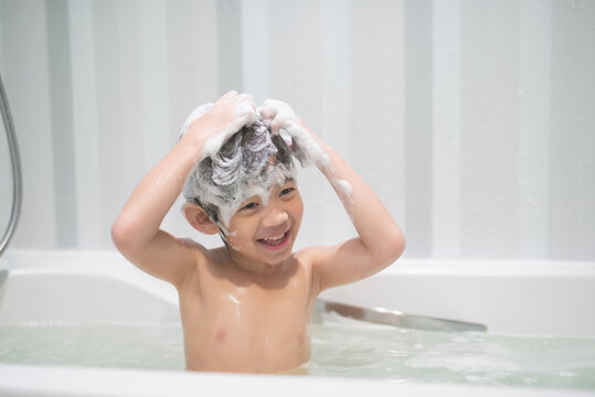 asian child washing in a bathroom in foam.