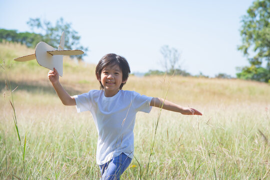 Asian child playing cardboard airplane in the meadow