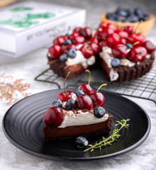 Delicious Nutella Dark chocolate tart, topped with with cherries and blueberries on the black plate.