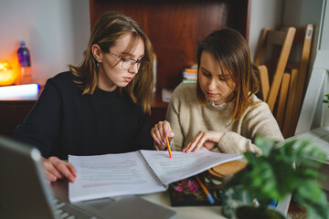 two women young caucasian female student sitting at home with her mentor teacher looking to the...