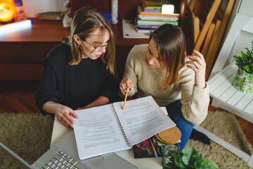 Fototapeta na wymiar two women young caucasian female student sitting at home with her mentor teacher looking to the notebook explaining lesson study preparing for exam learning education concept real people copy space