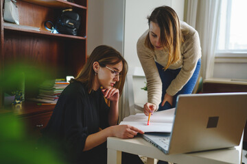 two women young caucasian female student sitting at home with her mentor teacher looking to the notebook explaining lesson study preparing for exam learning education concept real people copy space - obrazy, fototapety, plakaty