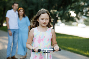 Obraz premium Girl on a scooter with family in a summer park.