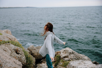 Fototapeta na wymiar beautiful woman in a gray sweater stands on a rocky shore nature Lifestyle