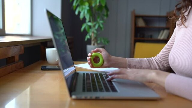Caucasian female office worker using expander working on laptop. Woman doing exercises for wrist diseases prevention from typing on computer. Tunnel syndrome injury and hand pain prevention concept