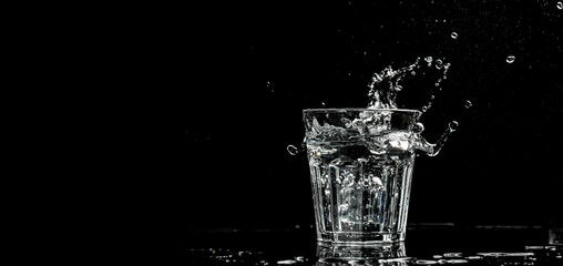 Close up view of the ice cubes splash in water are isolated on a black background. Long banner...