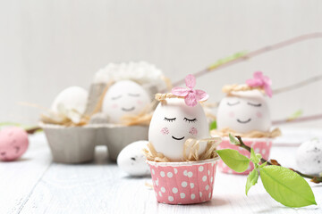 Easter holiday concept with cute handmade white eggs, tree branches, quail feathers and spring flowers on white wooden background.