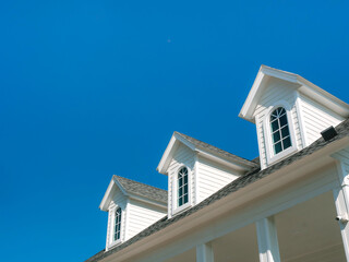 Three white vintage windows, little room decoration on the roof of the big white wooden house on blue sky background with copy space.