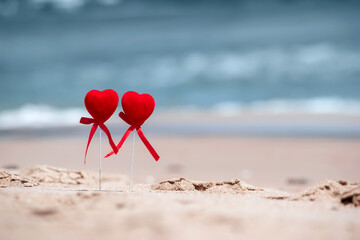 Fototapeta premium Romantic date loving couple on sea beach. Honeymoon trip, Happy Valentine's Day concept. Creative composition of two red hearts on the background of sea waves. Summer holidays background, copy space