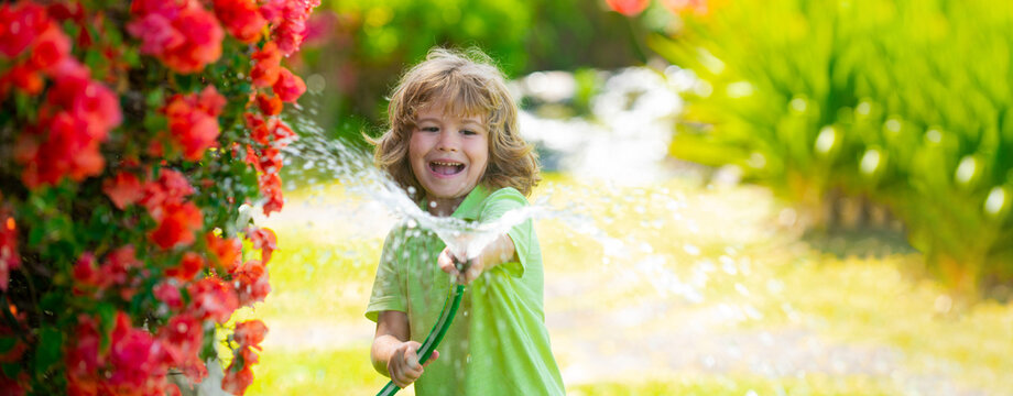 Banner with spring kids portrait. Adorable kid boy watering the plants, from hose spray with water hose in the garden at the backyard of the house on a summer evening.