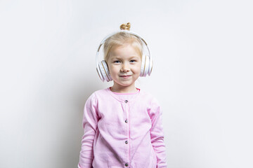 Smiling child girl in white headphones on a light background.