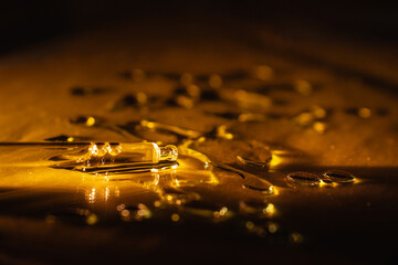 pipette and drops of spilled golden liquid on a dark background, illuminated by a warm beautiful...