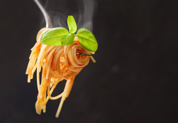 Pasta with tomato sauce and green basil on a fork