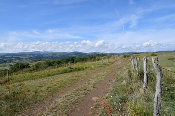 Petit chemin longeant une clôture dominant une vallée sur un plateau de montagne en Auvergne 